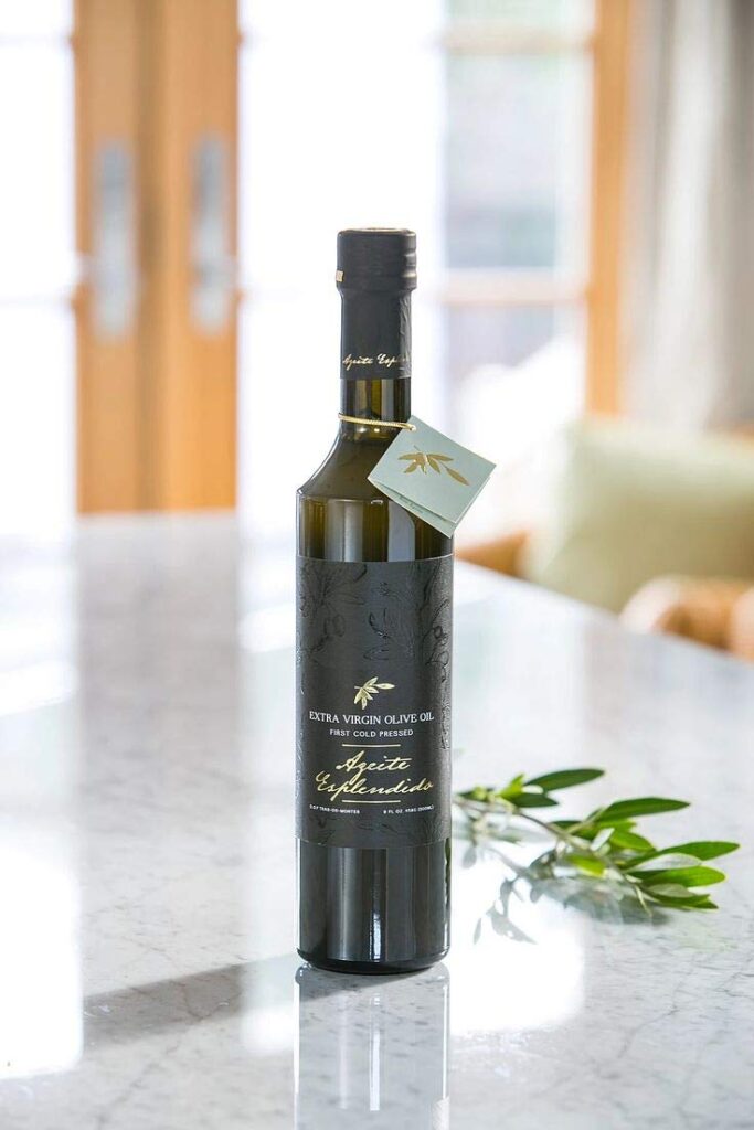 Bottle of Azeite Esplêndido extra virgin olive oil standing on a marble countertop with an olive branch beside it in a bright, sunlit kitchen