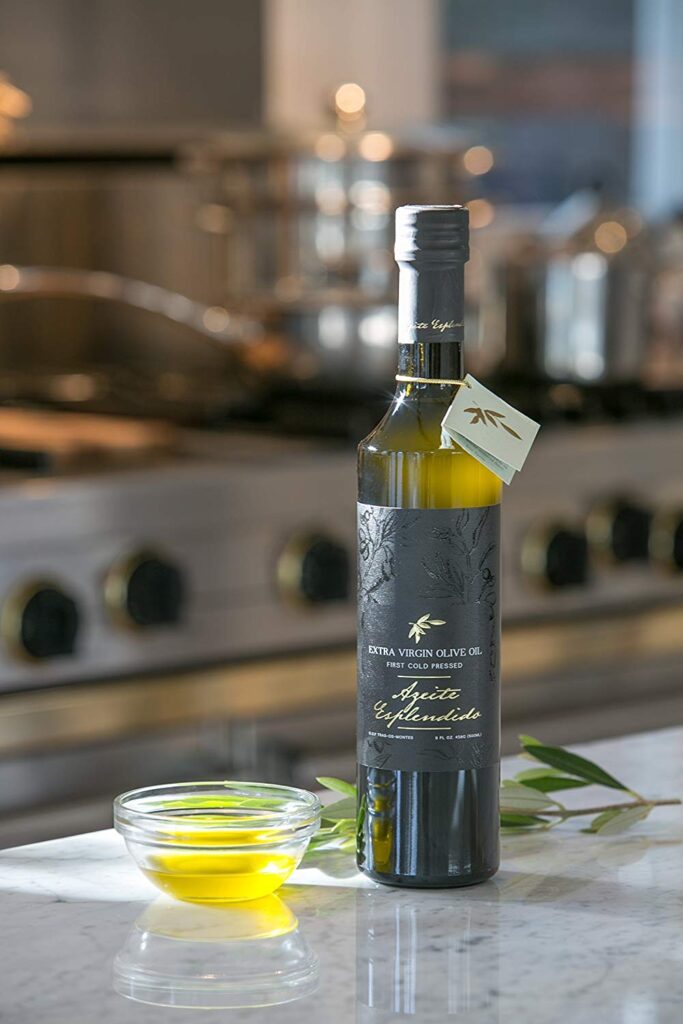 “Bottle of Azeite Esplêndido extra virgin olive oil on a marble kitchen countertop with a small glass bowl of olive oil and olive leaves, set against a modern kitchen background